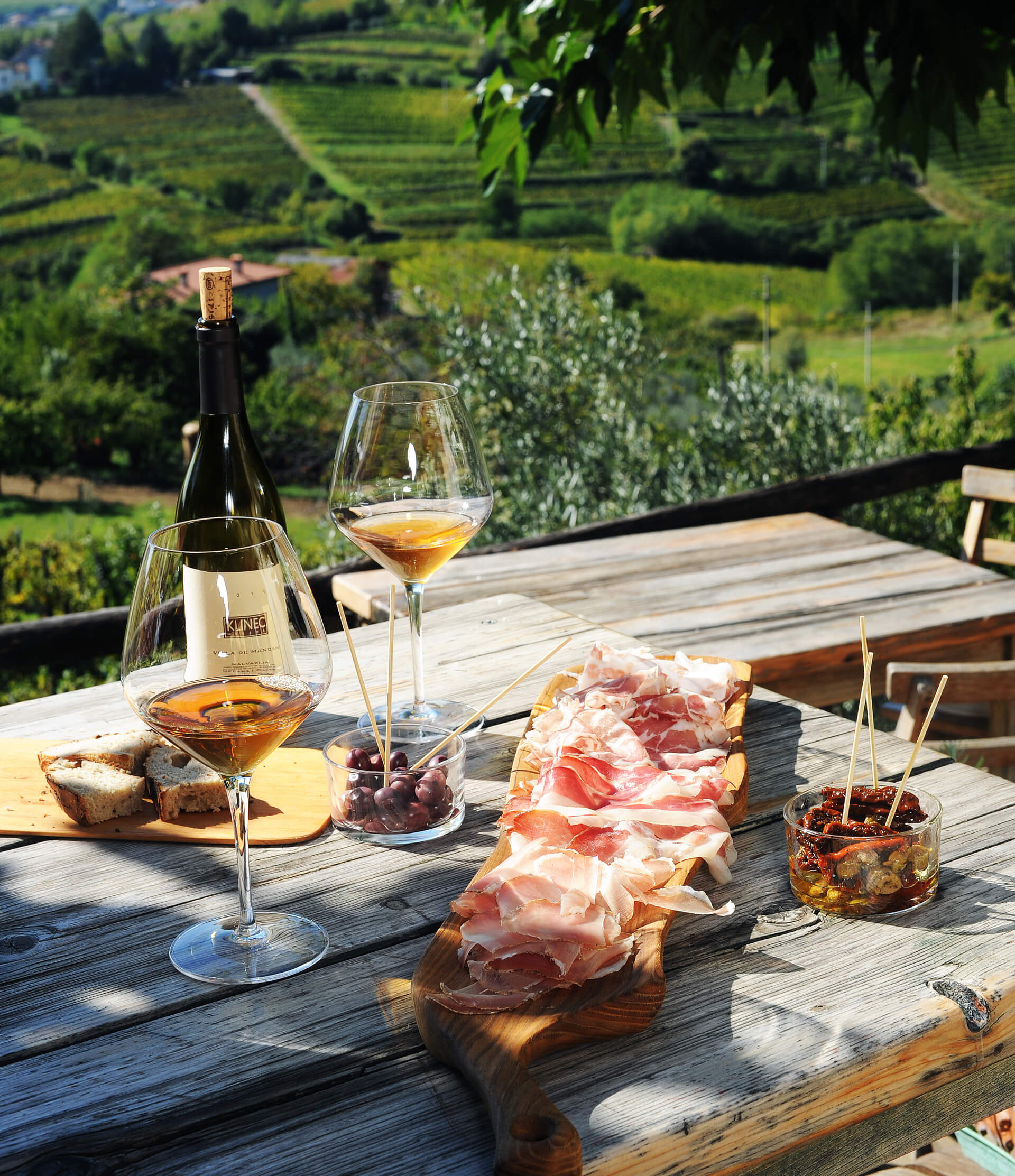Sunlit stone courtyard and terrace table with amber wine and house-cured Brda pršut at Domačija Klinec